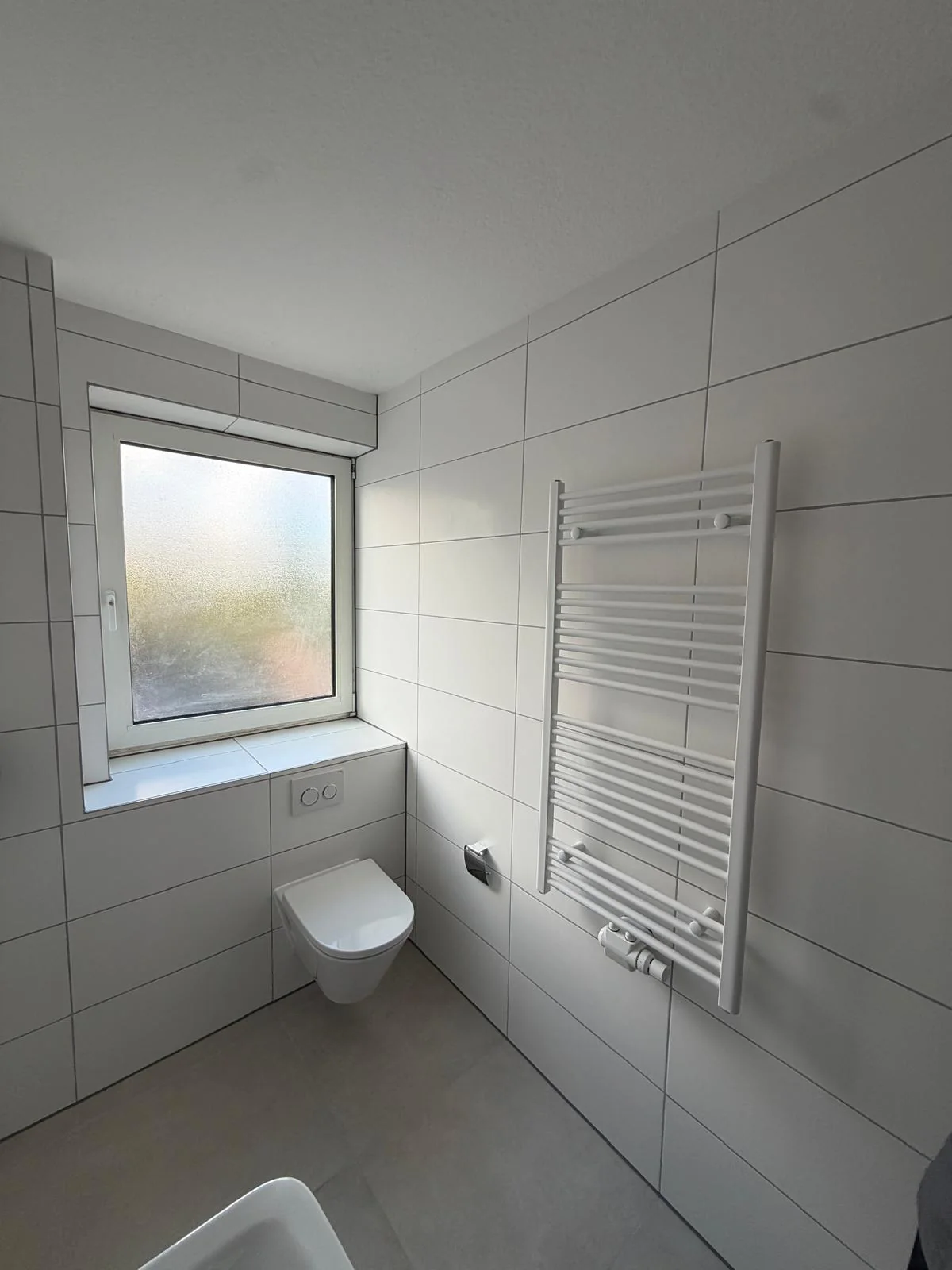 Saniertes Badezimmer mit hellen Fliesen, wandhängendem WC und Handtuchheizkörper
